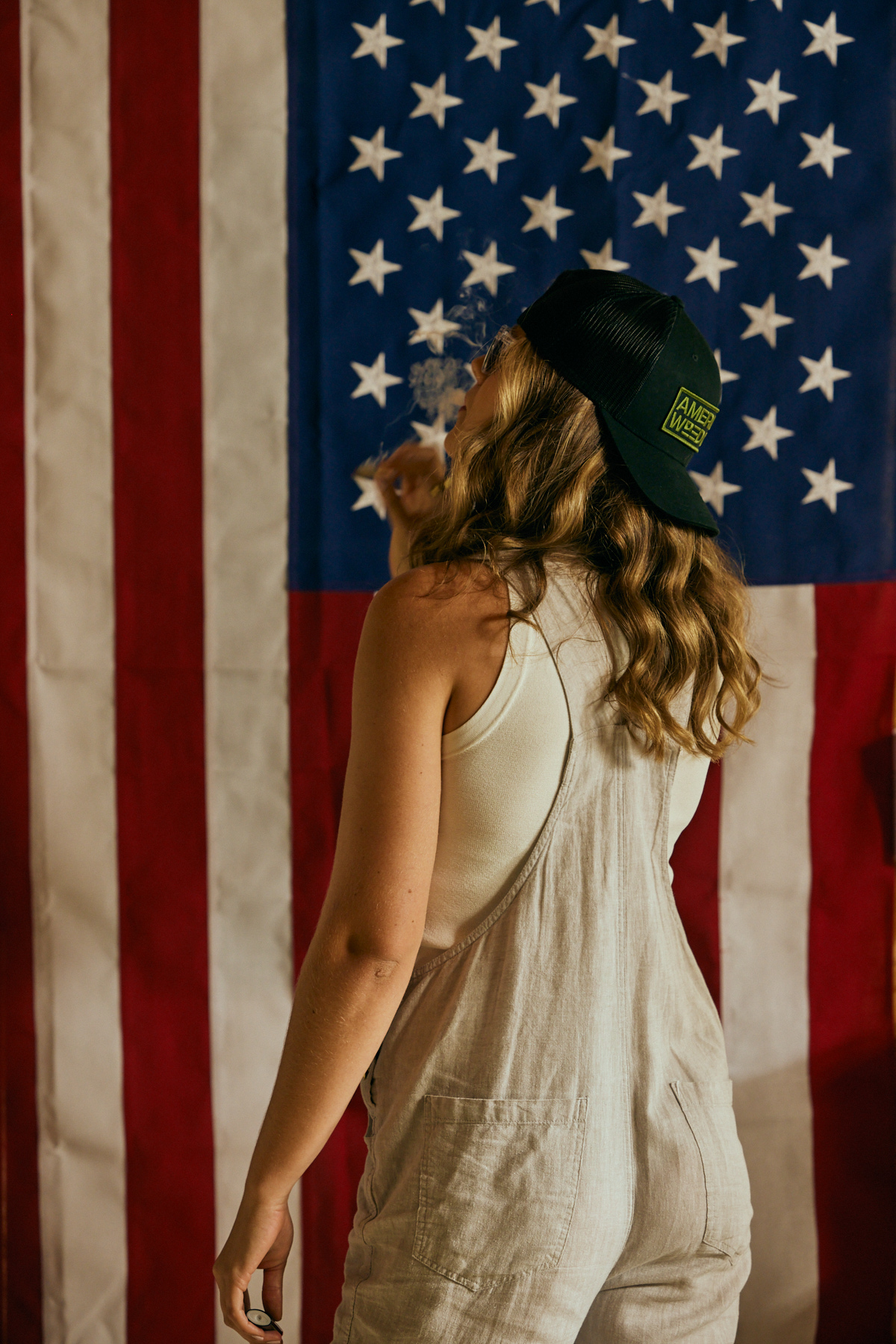 A woman smoking an American Weed Co cannabis preroll in front of an American Flag